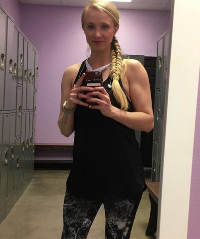 Woman with blonde, braided hair taking a selfie in a locker room with pink walls.