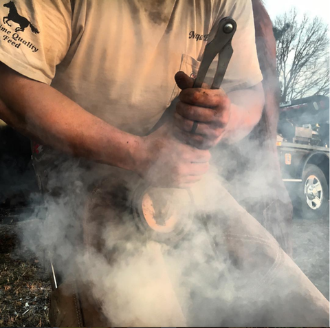 A man kneeling and working with a metal tool as it kicks up dust.