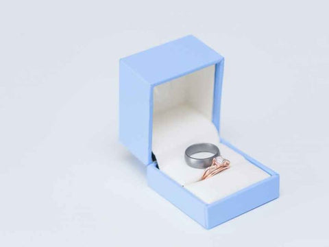 A bronze ring and a silver silicone wedding ring in a baby blue wedding ring box.