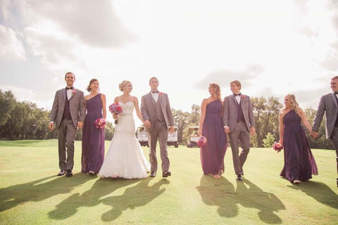 A man and wife walking on a green lawn with their best man and maid of honor.
