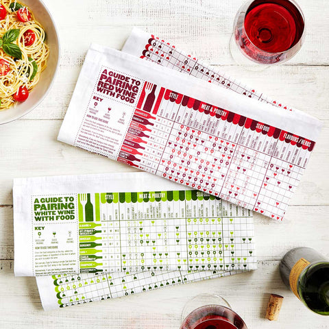 A set of wine pairing towels surrounded by glasses of red wine and a bowl of spaghetti.