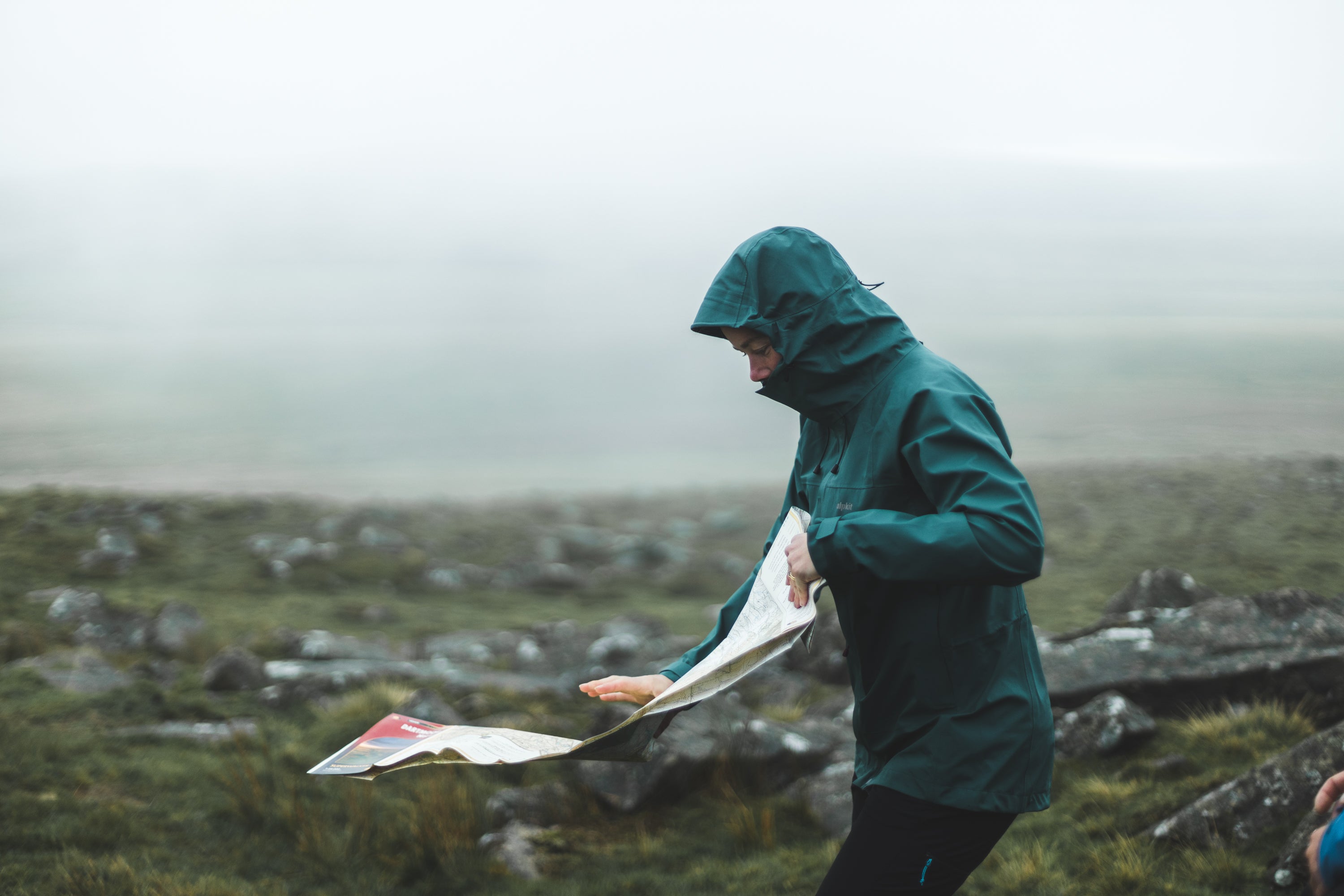 A woman unfolding a map in the rain on Dartmoor in a PFC free waterproof jacket