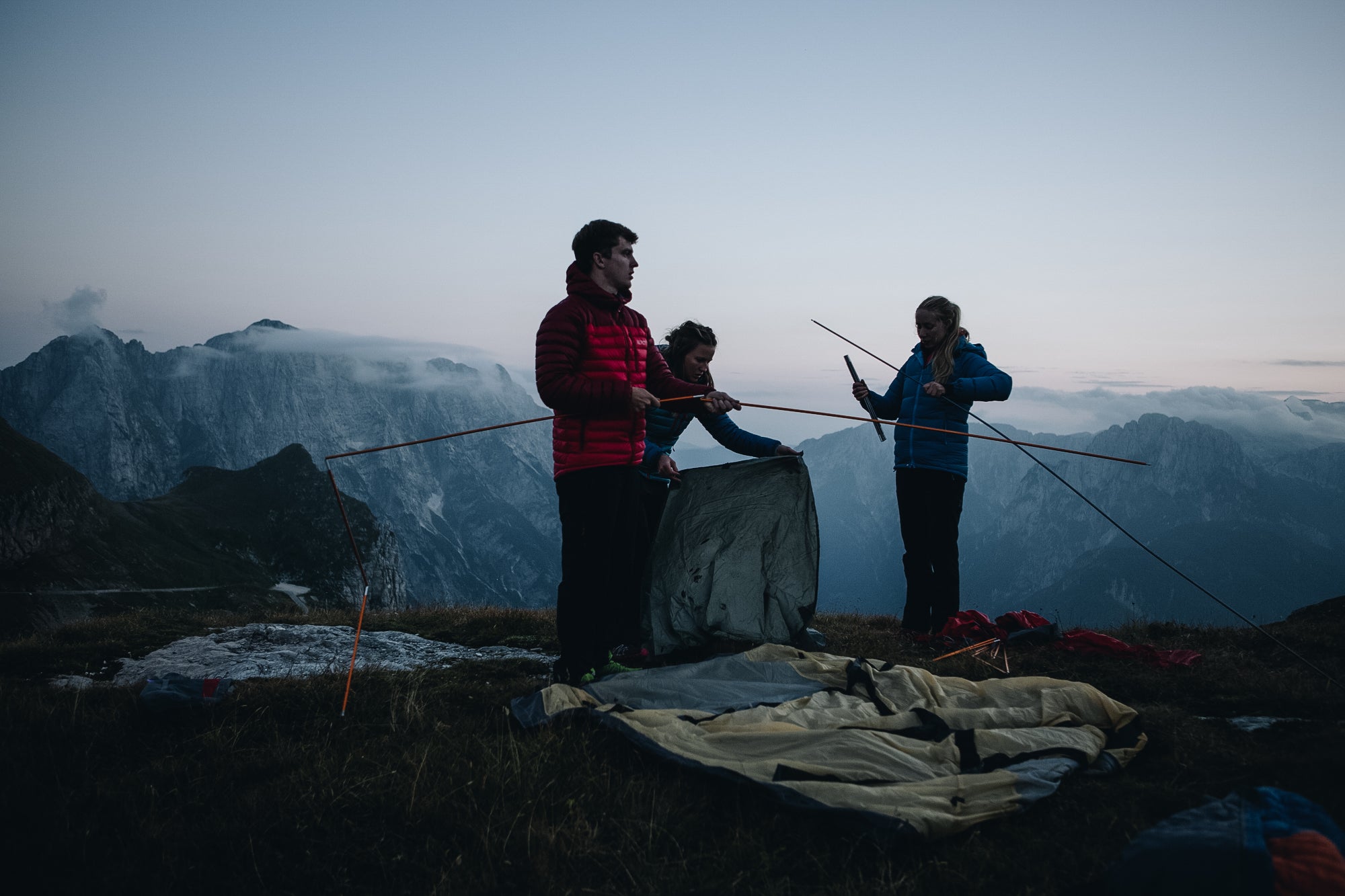 Three people putting the poles together for a 4 season mountain tent in the Slovenian mountains