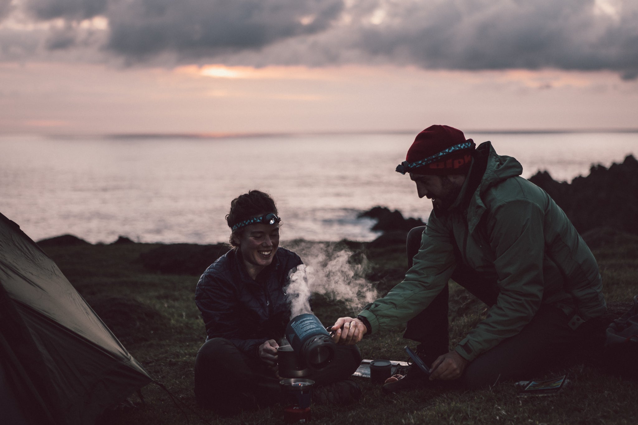 Two people camping and cooking dinner outside their tent on a camping stove