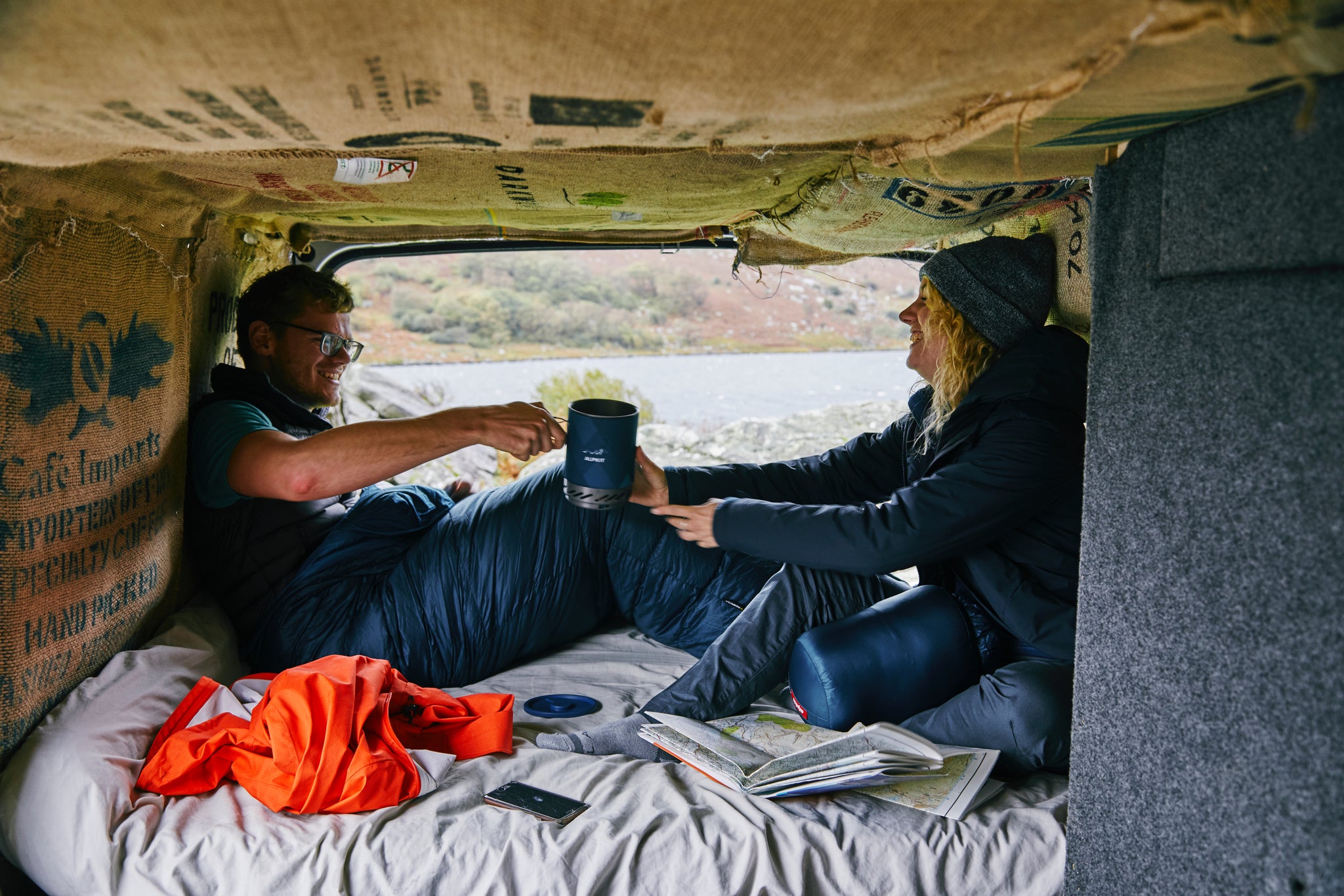 Two people sitting in sleeping bags in a van