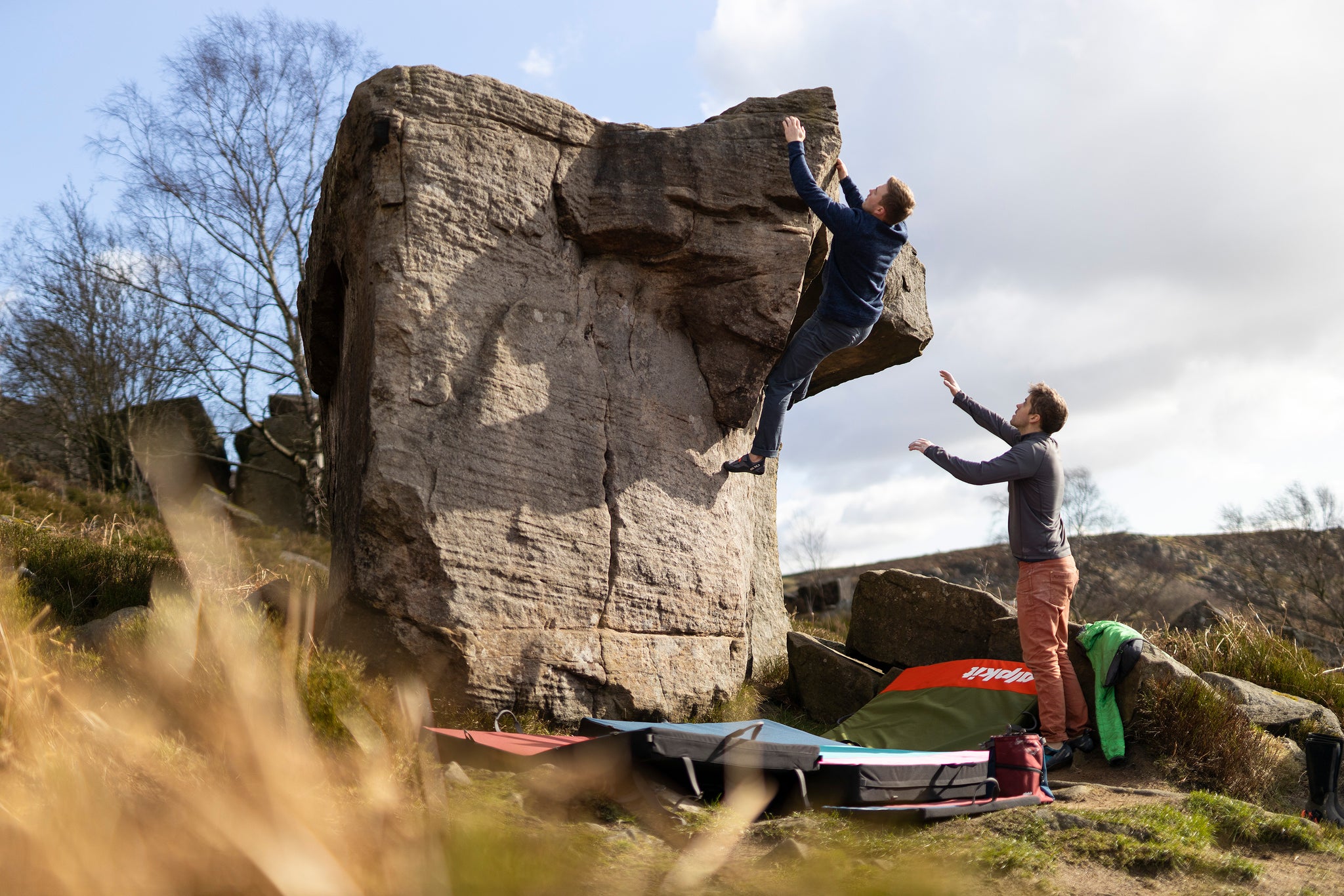 Two climbers on a bouldering problem in the Peak District National park with Alpkit crash pads