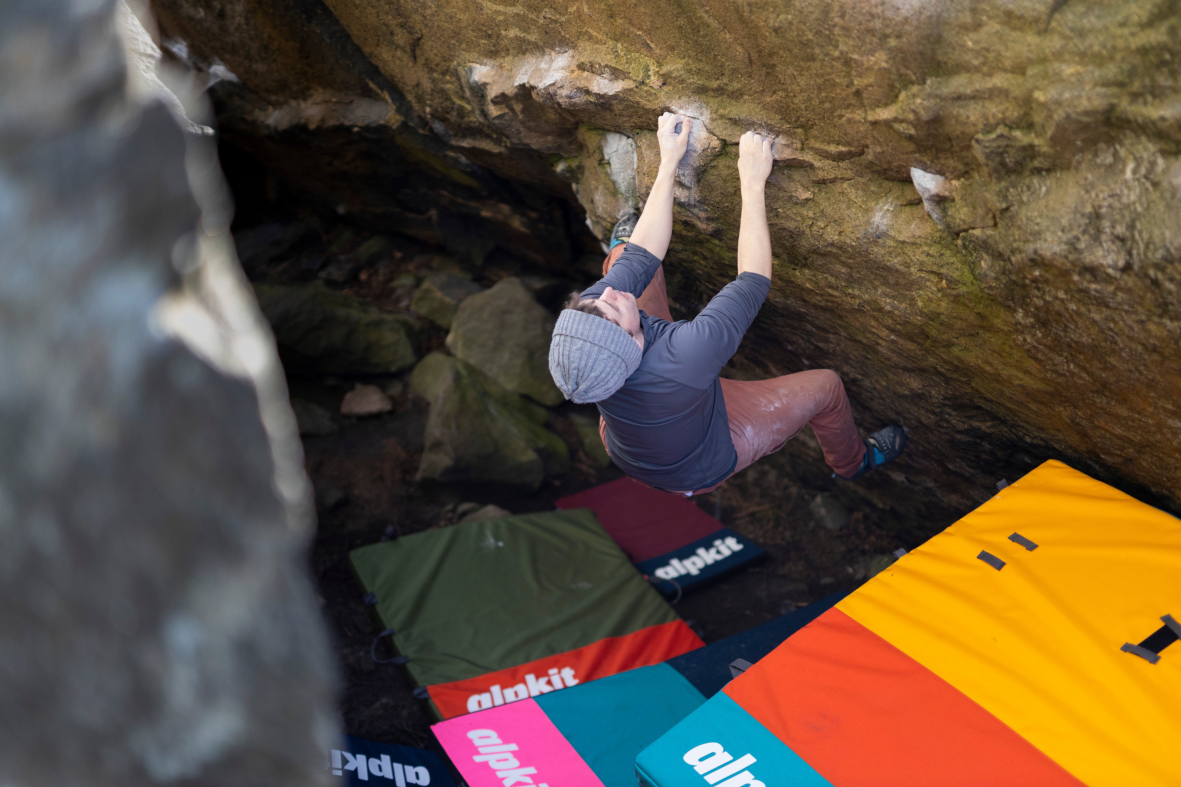 A climber bouldering in the Peak District above Alpkit UK made bouldering pads