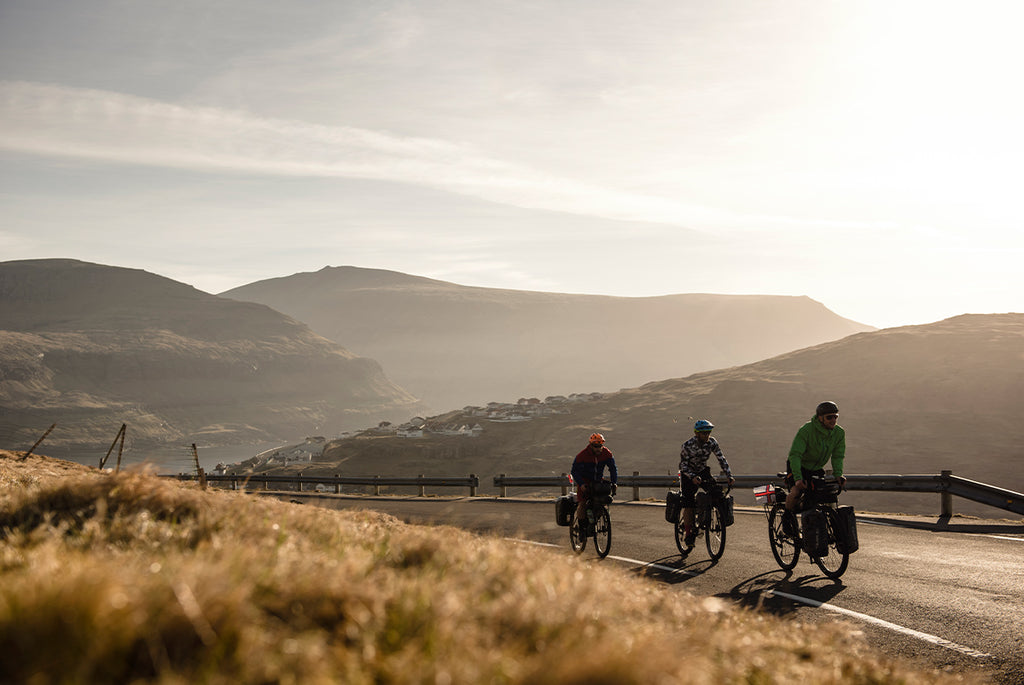 Three friends on touring bikes with panniers in the faroe islands as the sun is setting