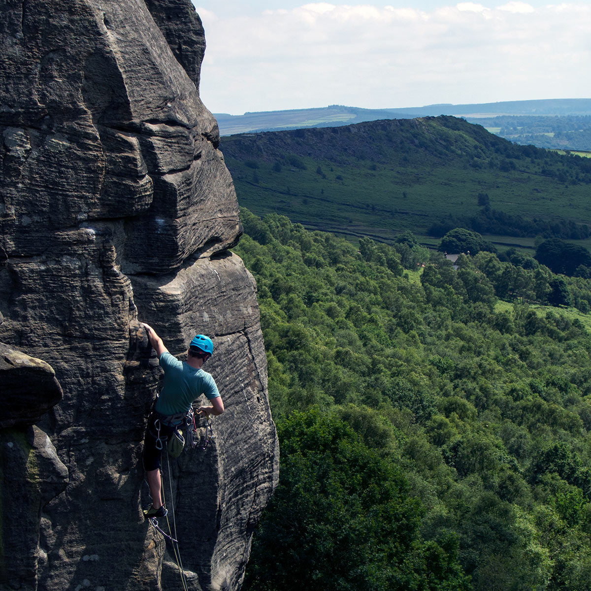 Climber high on exposed gritstone climb in the Peak District