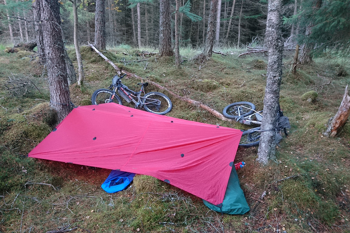 Bikepackers create bivvy with tarp stretched between two trees