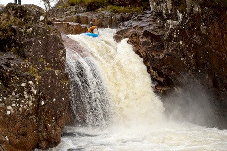 Kayaker in blue bloat going off the lip of a high waterfall