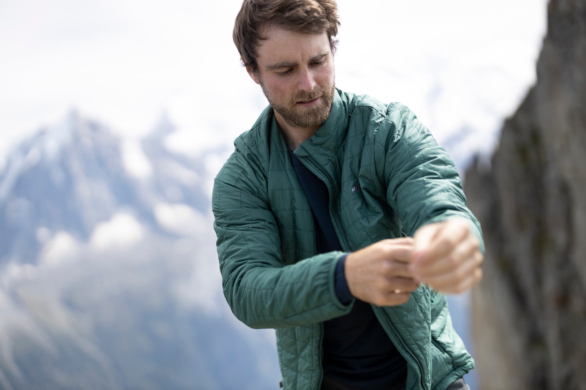 A man pulling on the Heiko Primaloft lightweight insulated jacket with quilted baffles