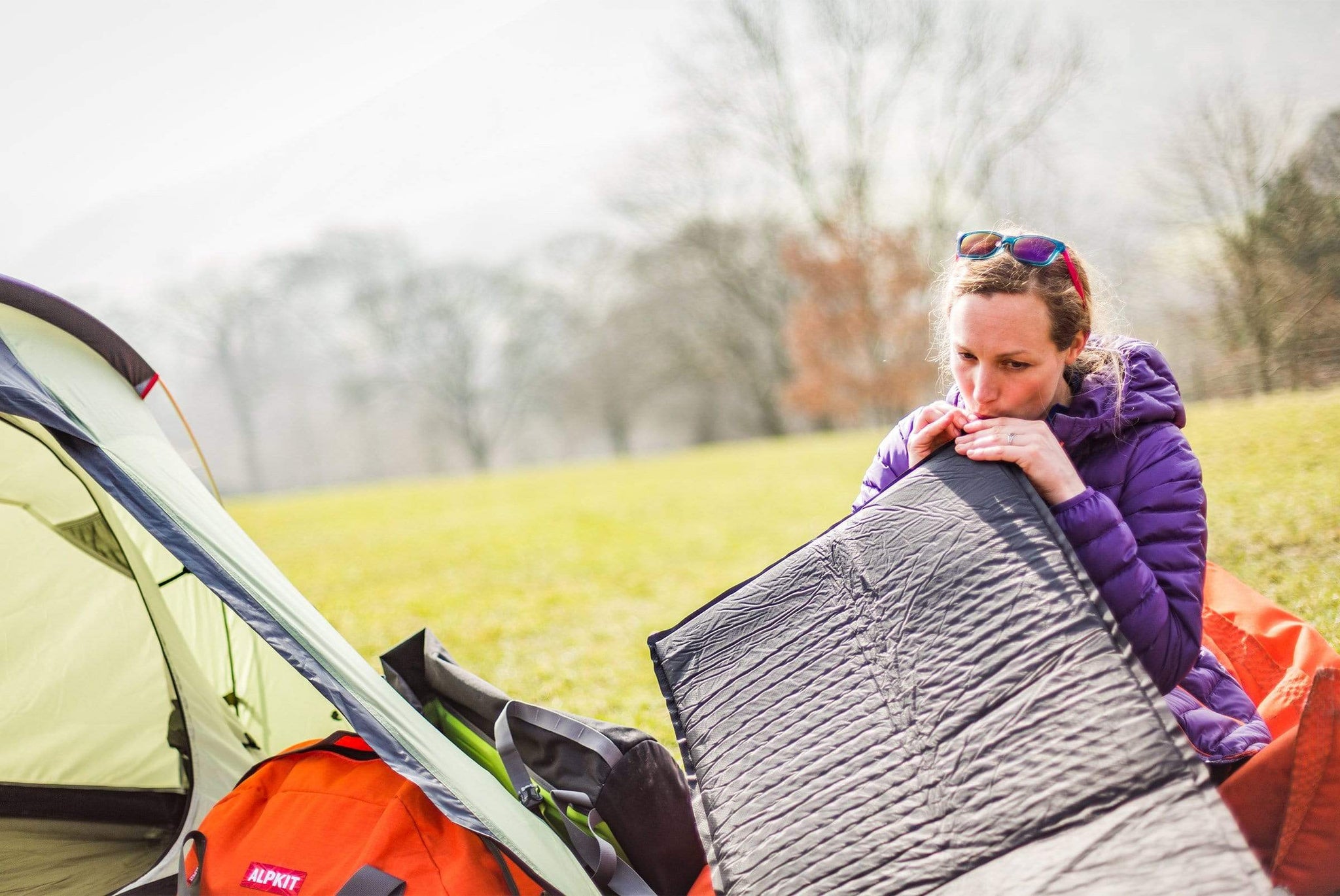 blåser in i en självuppblåsande sovmatta på en campingplats för att fylla på luften