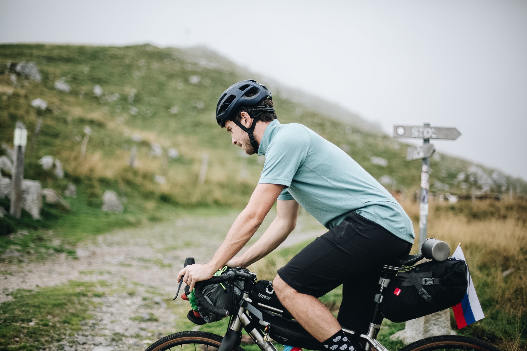 Man cycle touring on a gravel track in Slovenia, wearing a merino wool cycling jersey