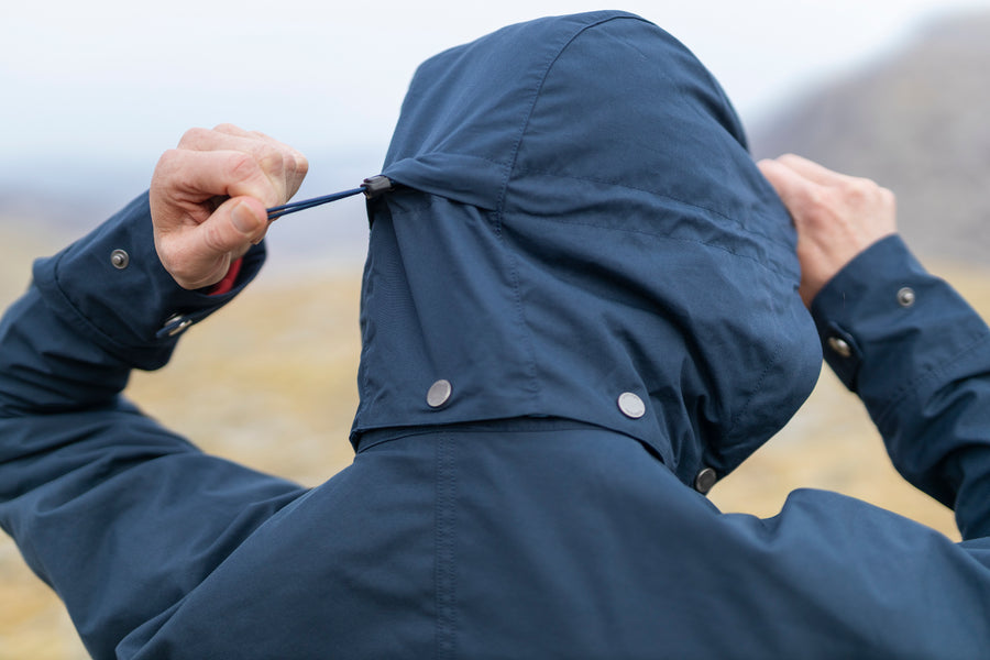 A woman pulling tight the adjustable removable hood on the navy Ranger Ventile jacket