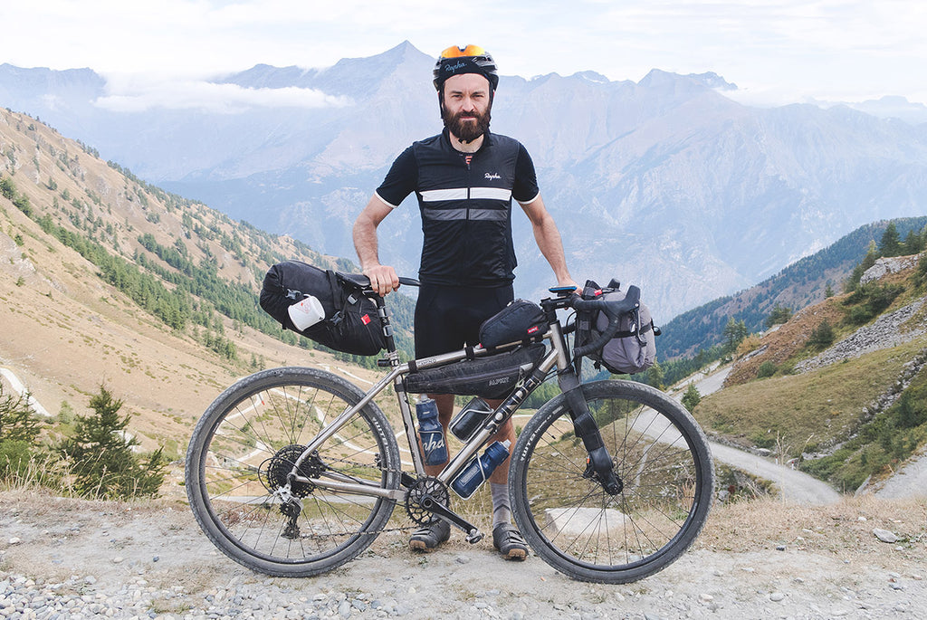 A man holding his sonder camino ti loaded up with bikepacking bags on a gravel path in the mountains