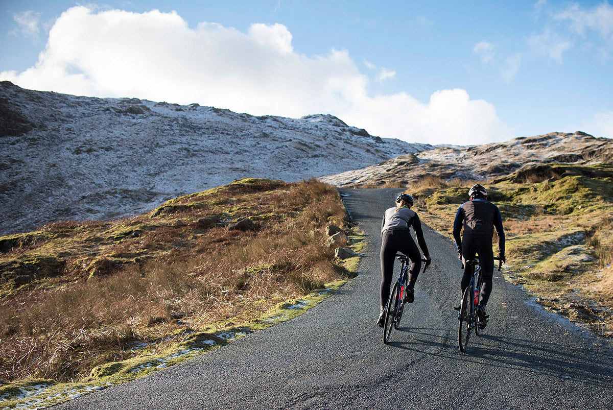 Two road cyclists climbing steep road in the snow