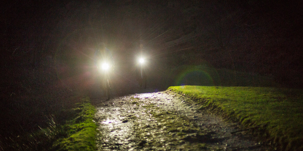 Two people cycling along a gravel path in the dark with bike lights on