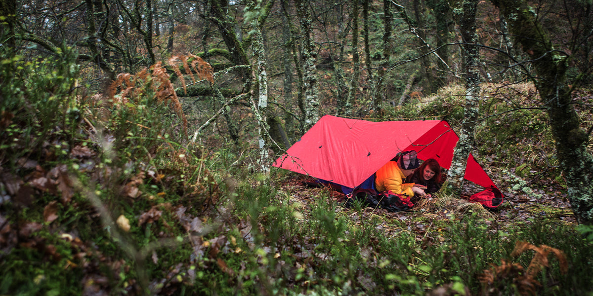 two people camping underneath a red tarp in the woods