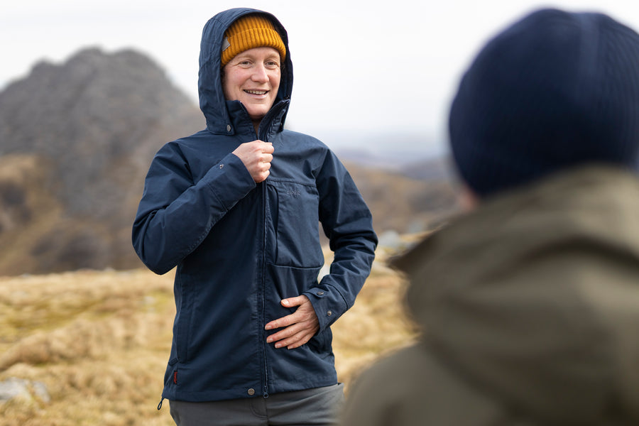 A woman zipping up a navy Ventile® jacket