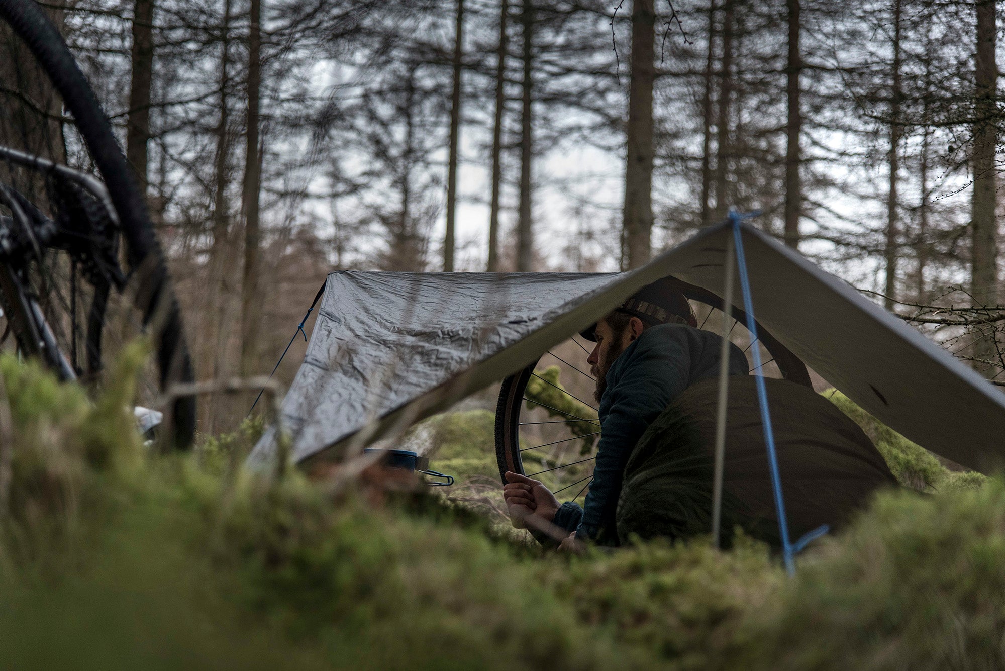 Man sleeping in a sleeping bag, in a bivvy bag, under a tarp, whilst bikepacking