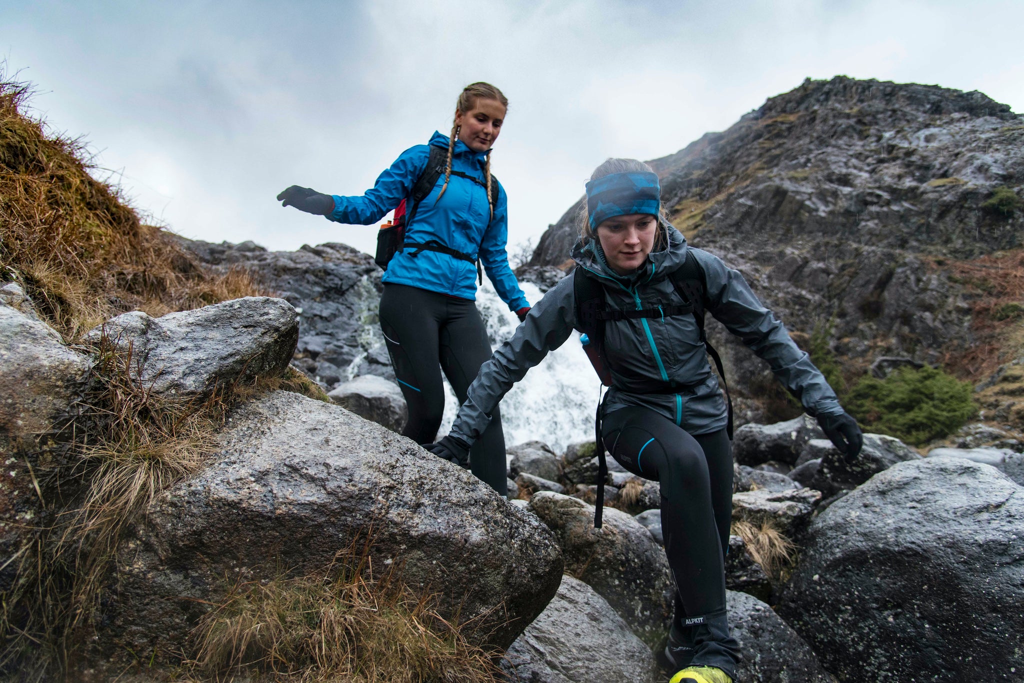 Two women running in the Lake District with rucksacks and waterproof jackets, training for a Mountain Marathon