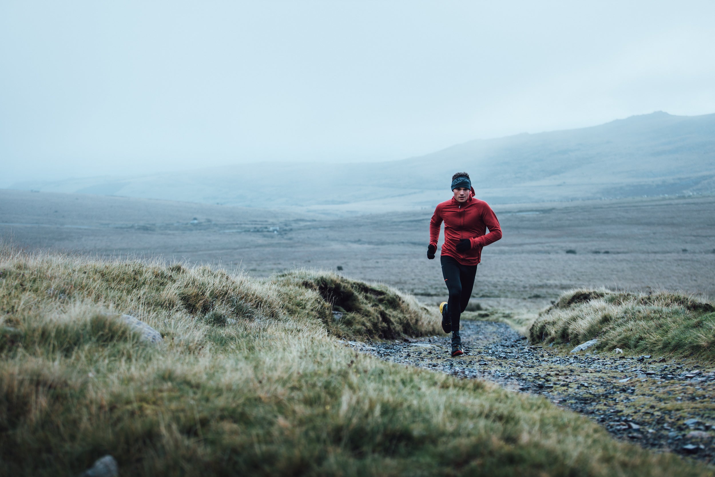 A man trail running across Dartmoor in winter in a fleece jacket and leggings