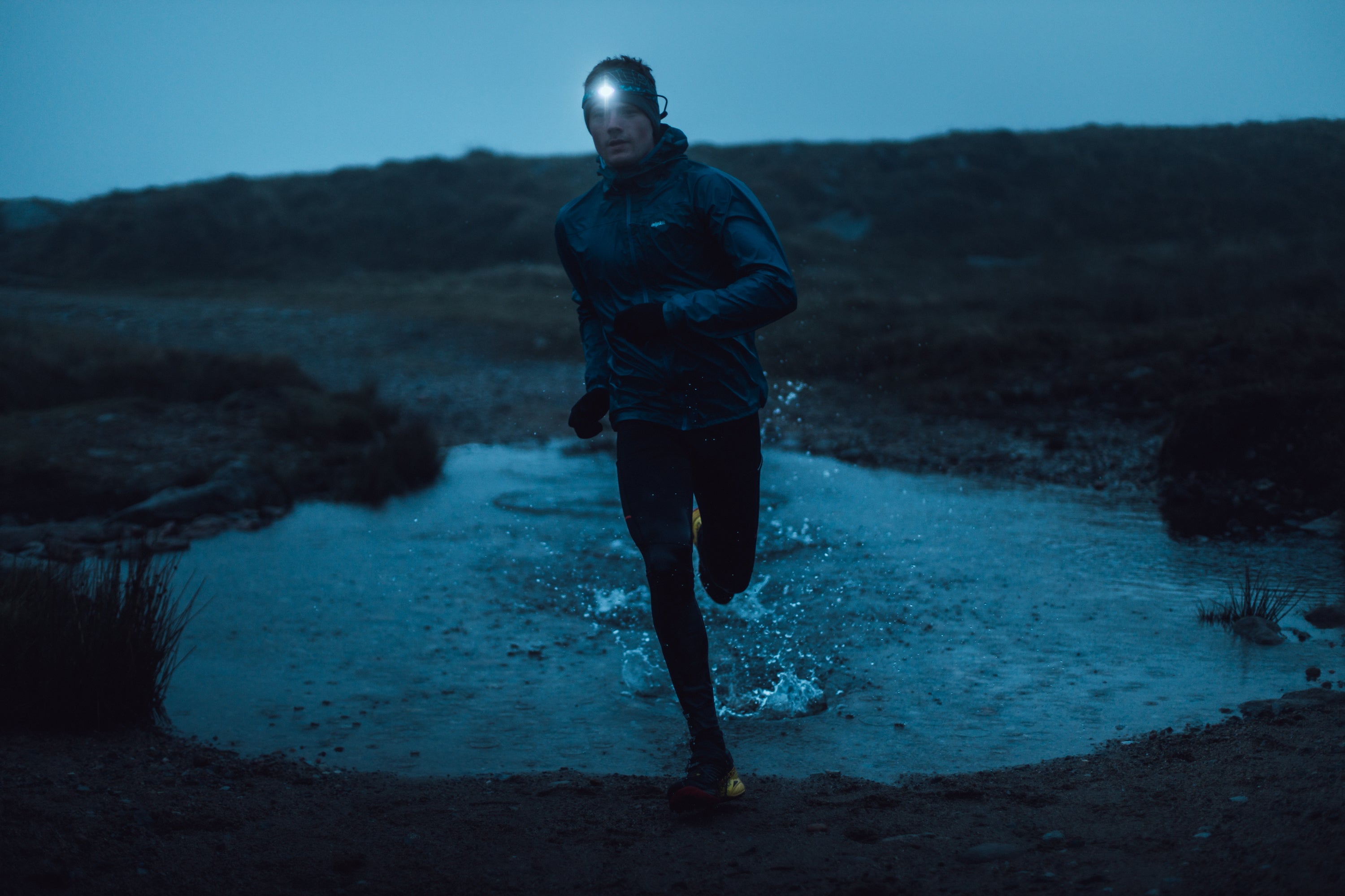 A man running through a puddle in winter with a head torch on