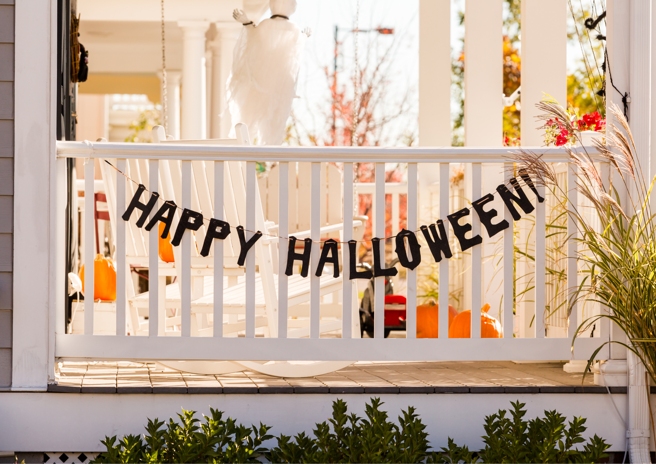 A white porch railing with a black garland that reads: Happy Halloween.