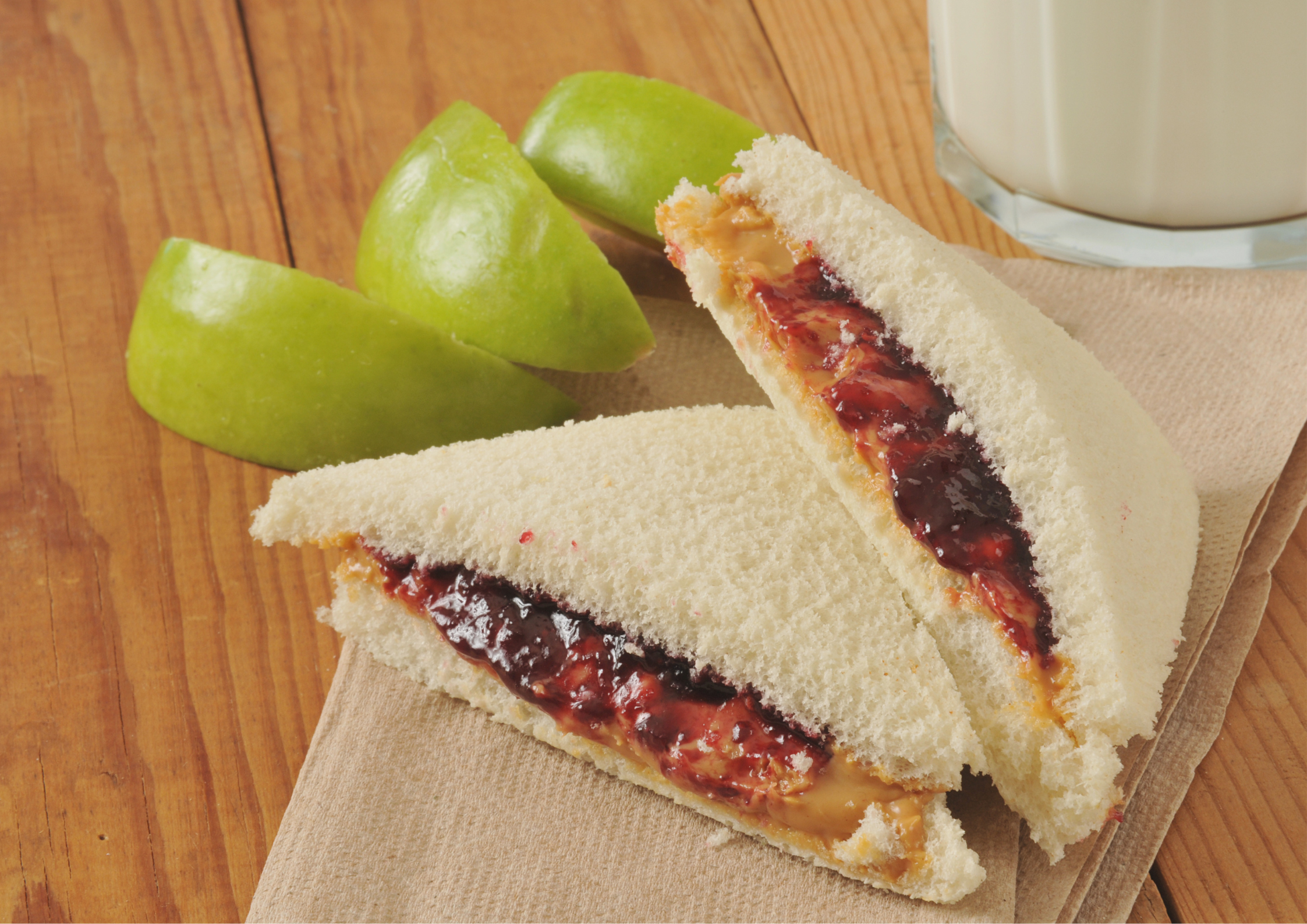 A peanut butter and jelly sandwich cut in half with the crusts cut off next to 3 pieces of a green apple cut up.