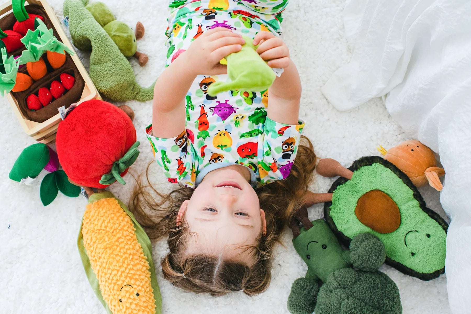 A little girl playing with plush veggies in her Birdie Bean pajamas