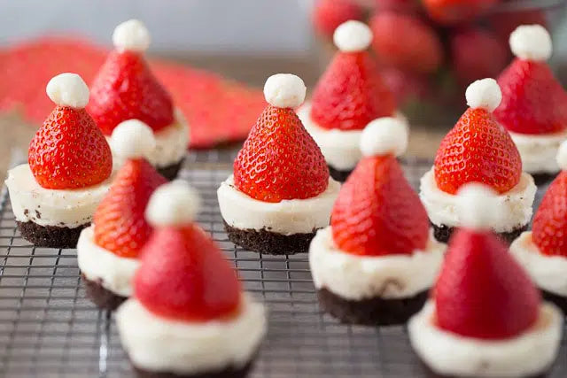 Mini no bake cheesecakes decorated to look like santa hats with strawberries and cream.