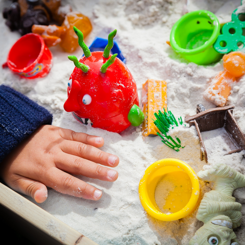 Child playing in a sandbox full of summer toys