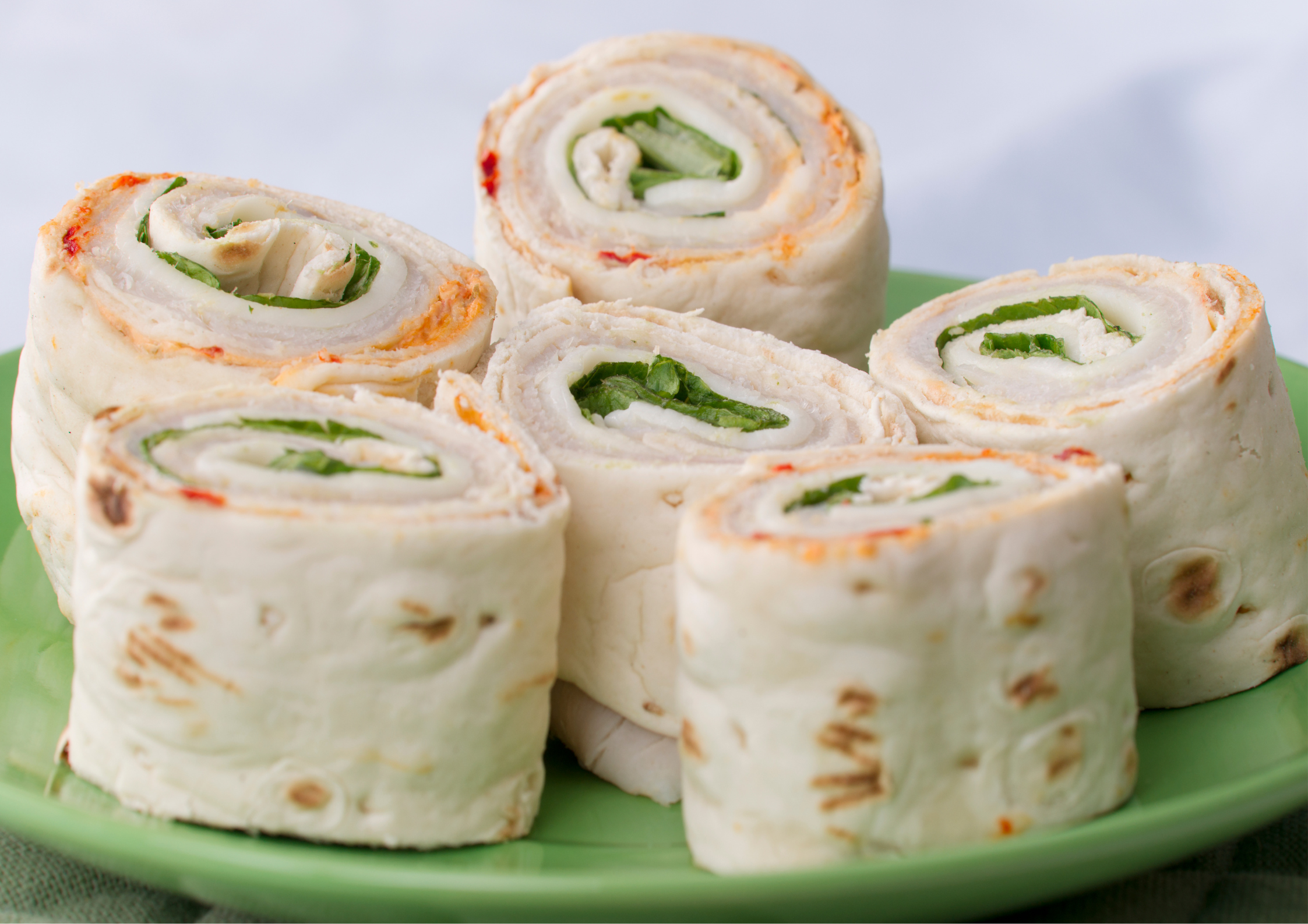 6 turkey, cheese and spinach pinwheels wrapped in tortilla shells on a green plate.