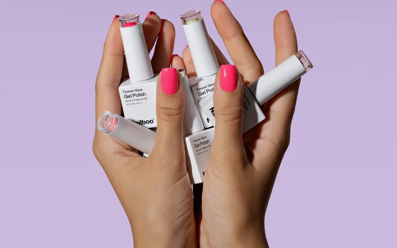 Hands with pink nails holding multiple bottles of white gel nail polish.