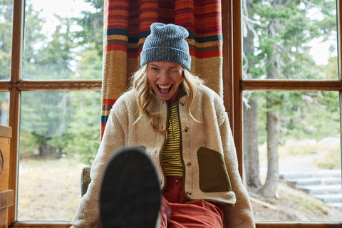 happy woman in a cozy cabin wearing the Toad&Co Sespe Jacket