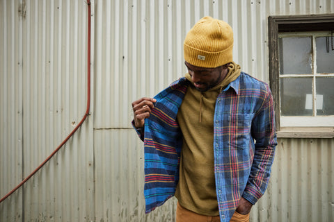 Man in a flannel and beanie against a wall