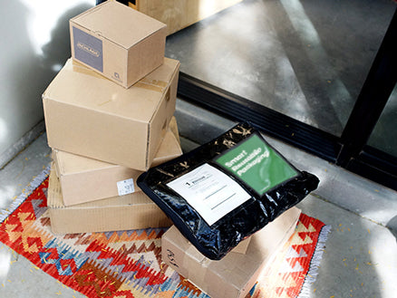 Cardboard packages stacked next to a LimeLoop reusable shipper on a doorstep