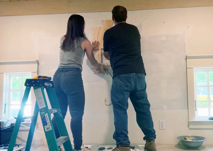 Lena and her dad fit the back panel of the range hood to the wall before assembly