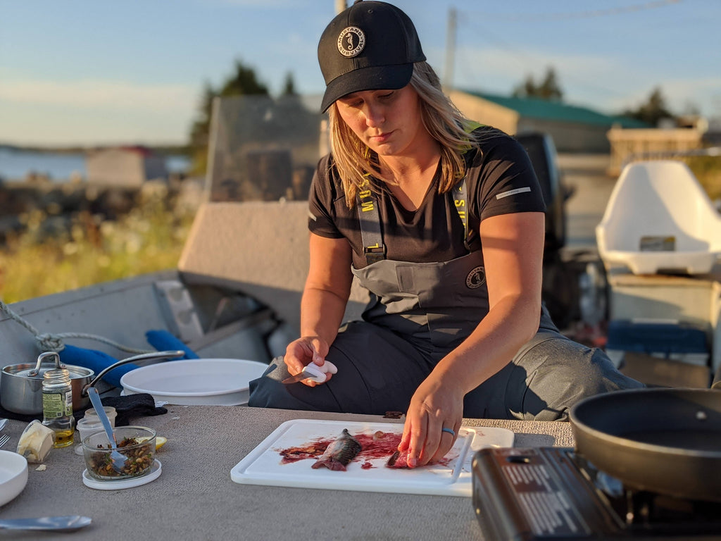 young woman on a boat cutting and gutting fresh fish to cook 