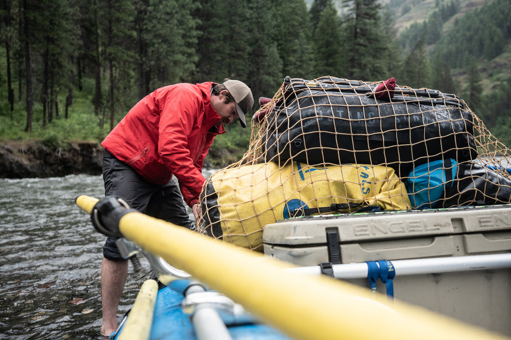 man in red waterproof jacket loading up river raft 