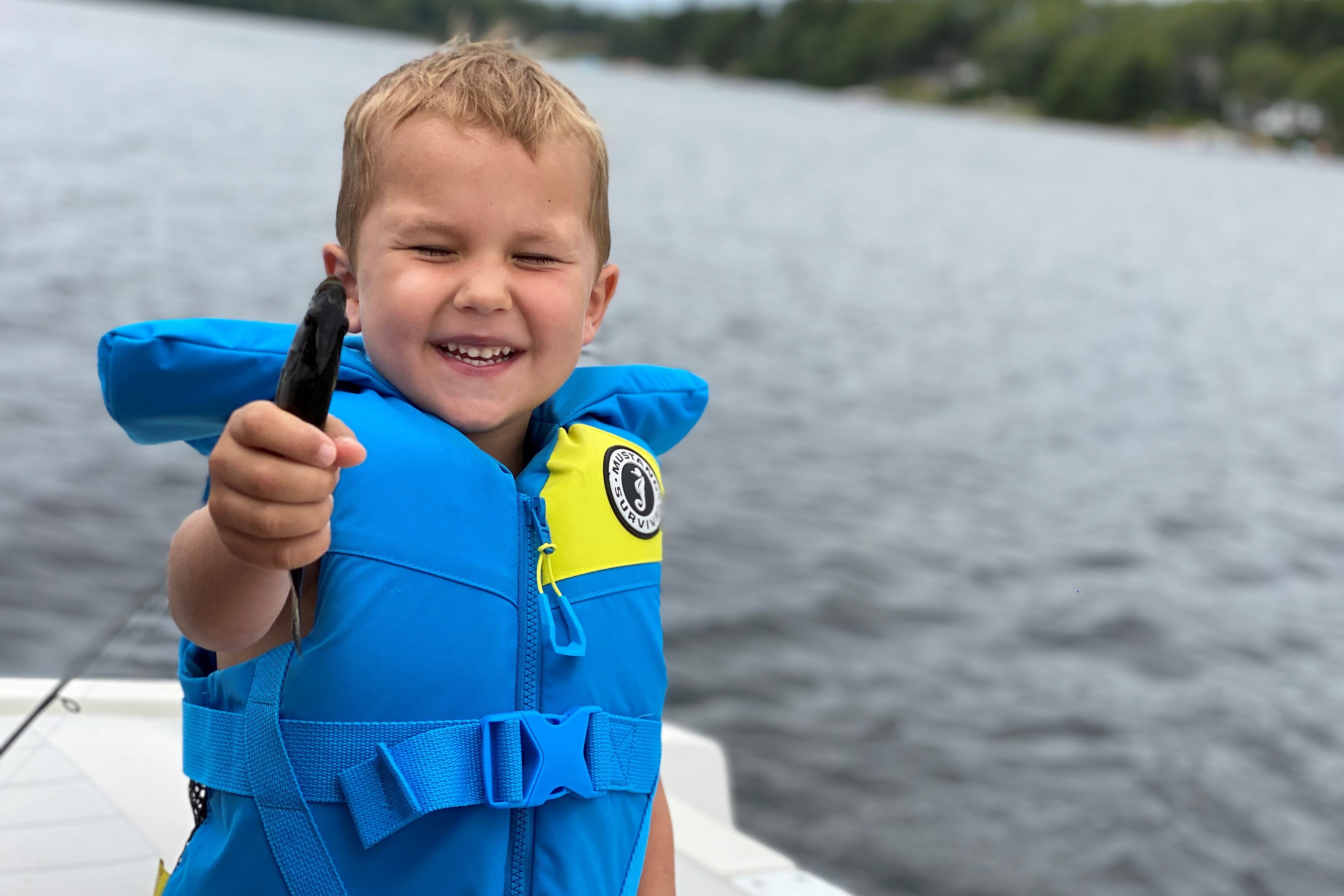 young boy excited about fish he has in his hand, wearing blue childs PFD