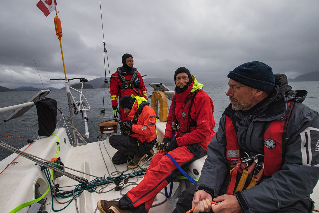 three men in foul wether gear on deck of sailing boat on cloudy day 