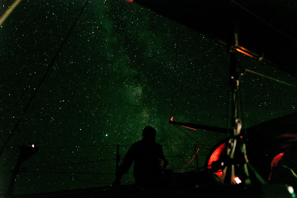woman gazing up at night sky full of stars from aboard a sail boat 
