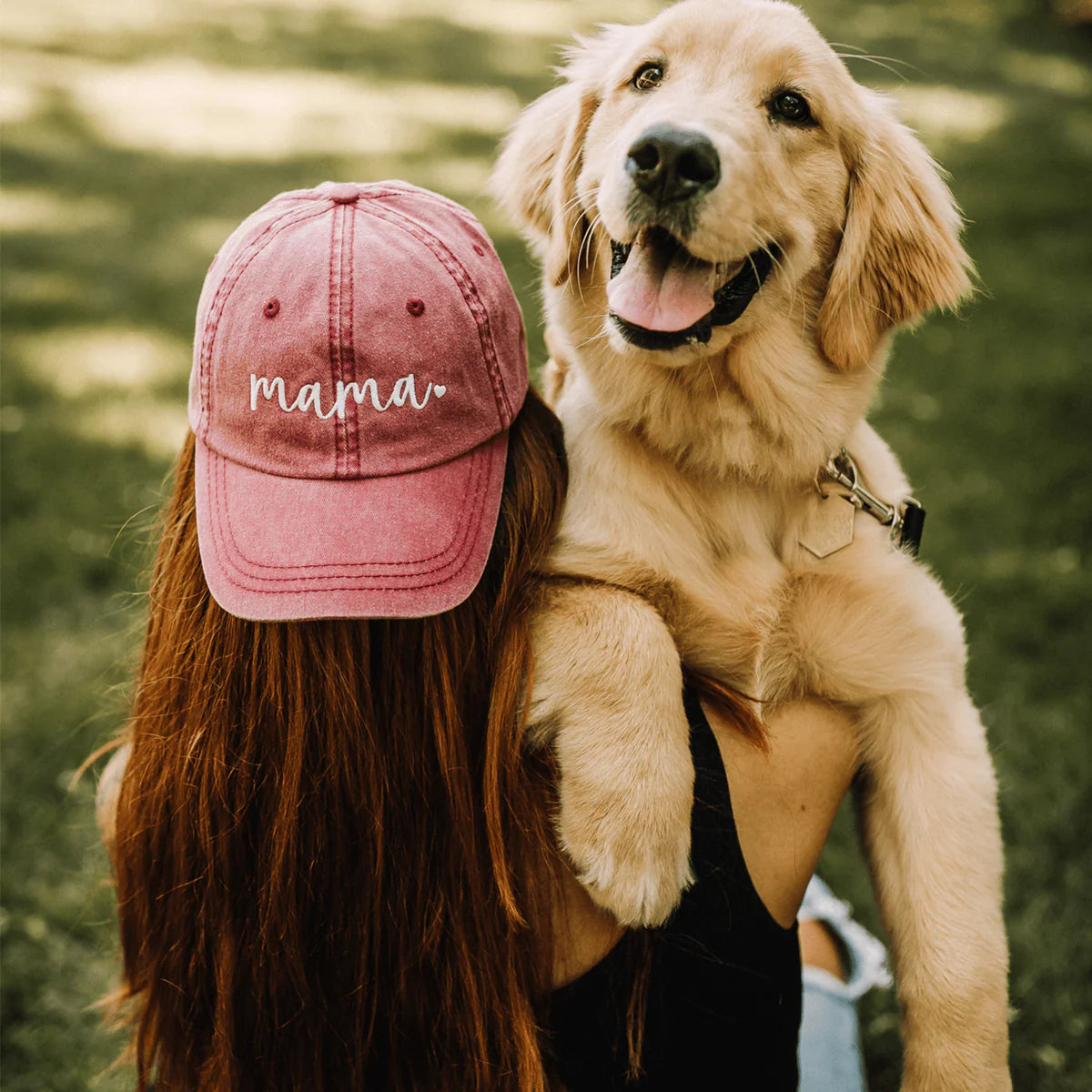 A woman wearing a trucker hat that says Mama and holding a dog