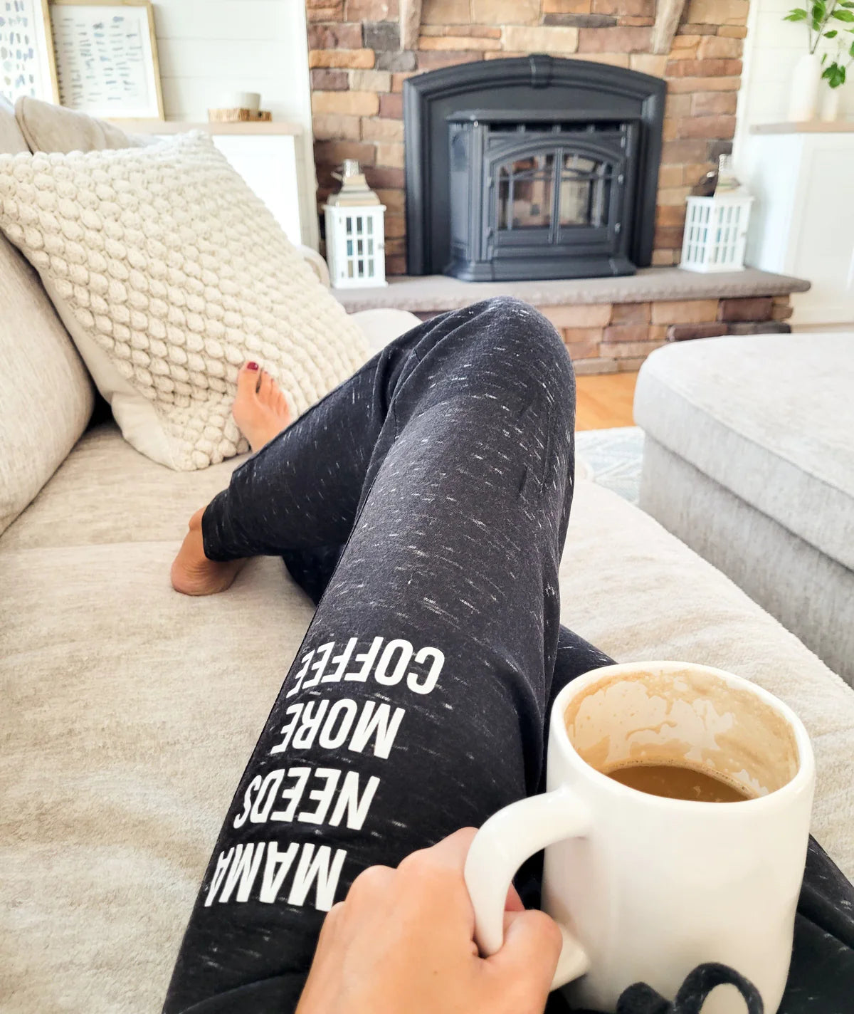A mom wearing lounge pants and drinking coffee on the couch