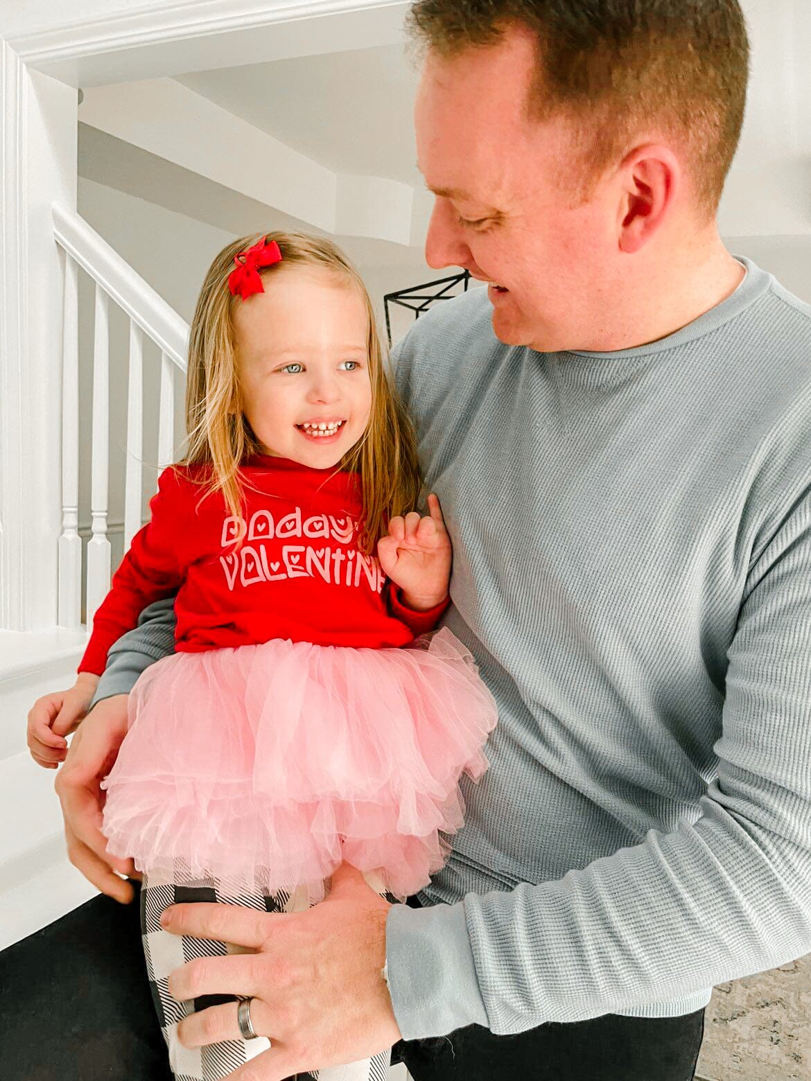 a dad holding his daughter, who is wearing a Valentine’s Day shirt and tutu