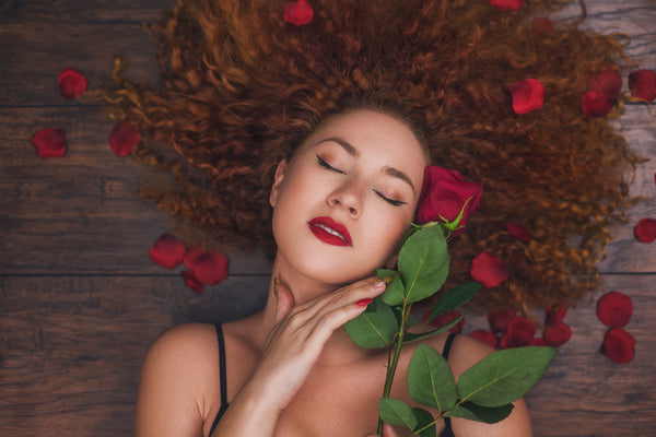 Beautiful woman enjoying a romantic moment at home while celebrating Valentine's Day with a red rose in her hand