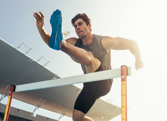 Male athlete jumping over hurdle