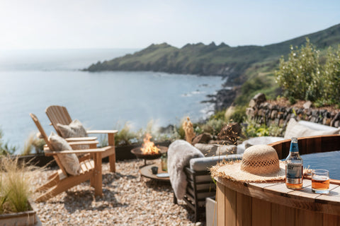 Photograph of the sunny outdoor space at Ukiyo, a private oasis with traditional wooden clad hot tub, furniture around a burning fire pit and exceptional sea views.